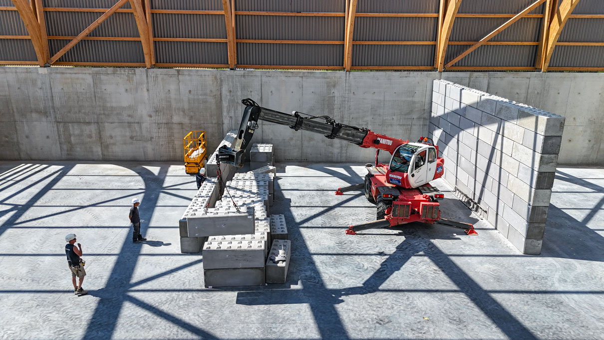 engin de levage déplaçant les blocs de béton pour créer des alvéoles de stockage dans le bâtiment.